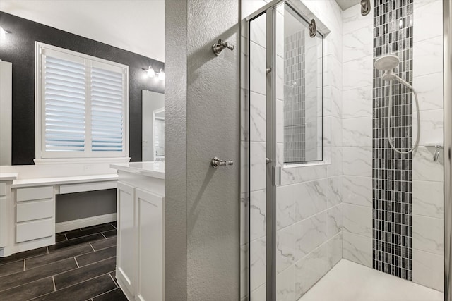 bathroom featuring a textured wall, vanity, wood finish floors, and a stall shower
