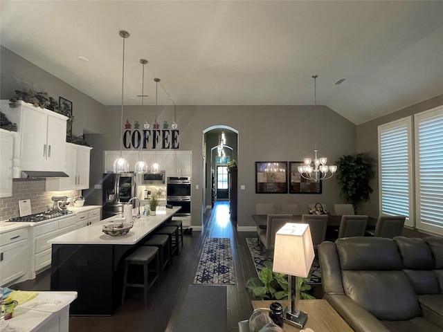 living area with a chandelier, dark wood-style floors, baseboards, arched walkways, and vaulted ceiling