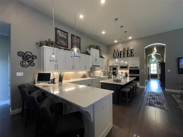 kitchen featuring tasteful backsplash, appliances with stainless steel finishes, light countertops, arched walkways, and a kitchen bar
