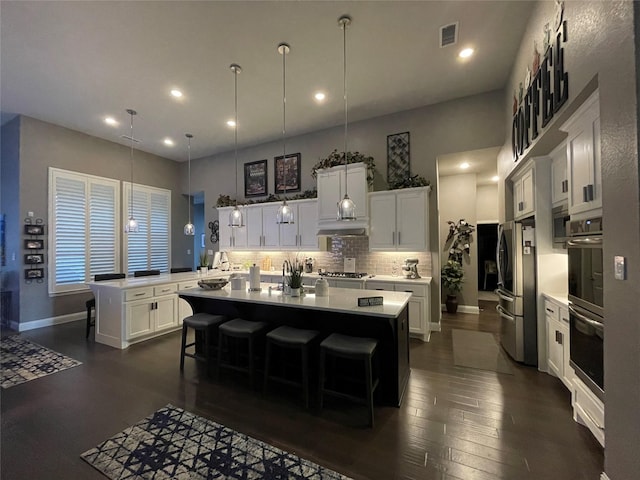 kitchen featuring an island with sink, decorative backsplash, appliances with stainless steel finishes, light countertops, and visible vents