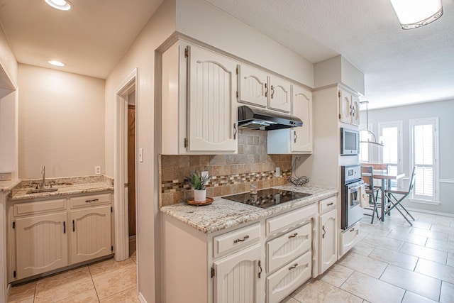 kitchen featuring sink, built in microwave, light stone countertops, black electric cooktop, and stainless steel oven