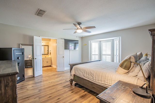 bedroom with ensuite bathroom, ceiling fan, a textured ceiling, and light wood-type flooring