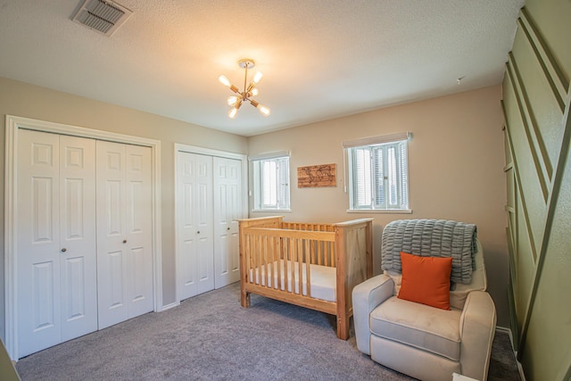 bedroom with multiple closets, carpet flooring, a textured ceiling, and a chandelier