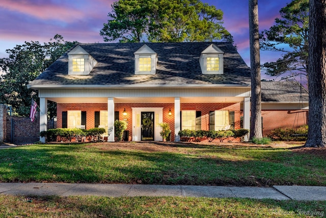 cape cod house with a front yard, brick siding, and roof with shingles