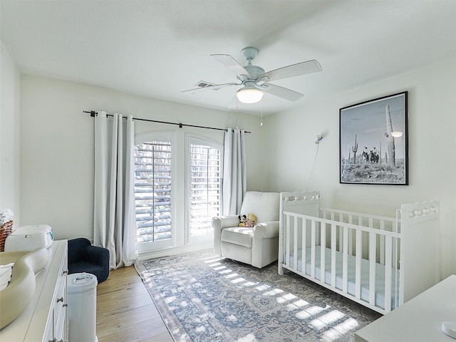 bedroom featuring ceiling fan, a nursery area, and hardwood / wood-style flooring