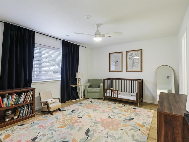 bedroom with ceiling fan, light hardwood / wood-style floors, and a crib