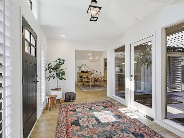 foyer entrance with french doors, light hardwood / wood-style flooring, vaulted ceiling, and a notable chandelier