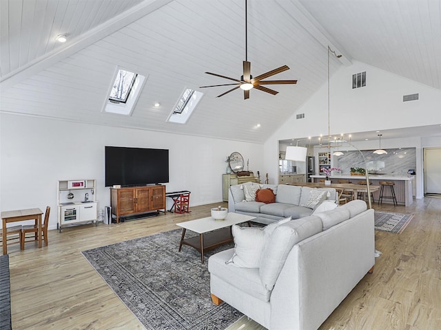 living room with light wood-type flooring, a skylight, ceiling fan, beam ceiling, and high vaulted ceiling