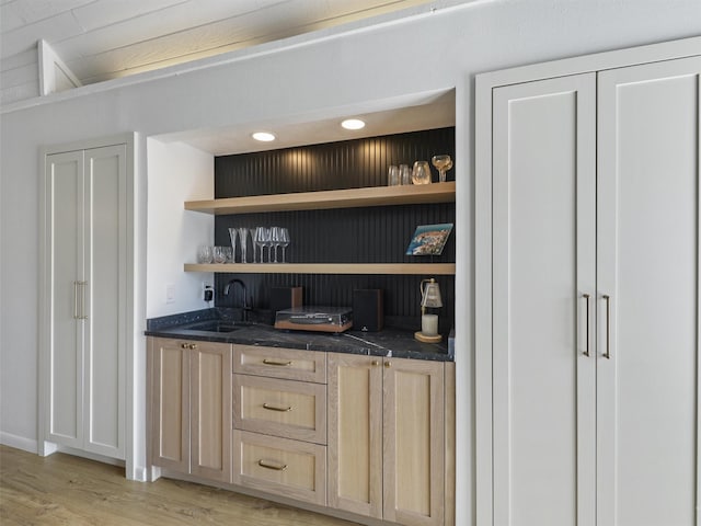 bar with light brown cabinetry, sink, and light wood-type flooring