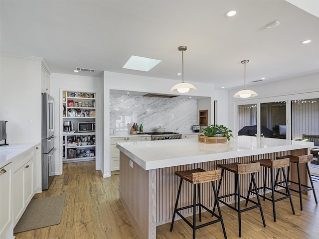 kitchen featuring decorative backsplash, a kitchen bar, a spacious island, white cabinets, and hanging light fixtures