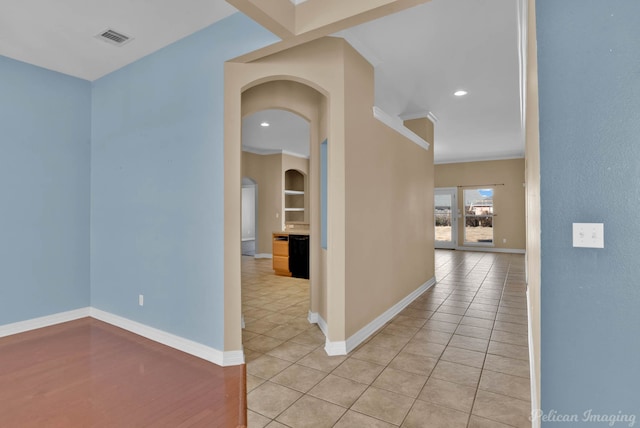 corridor featuring light tile patterned flooring, crown molding, and built in shelves