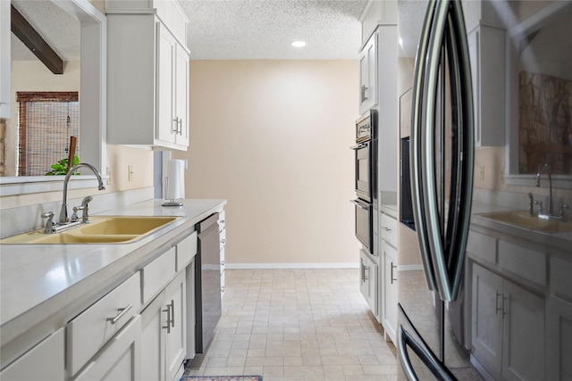 kitchen with beam ceiling, white cabinetry, sink, stainless steel appliances, and a textured ceiling