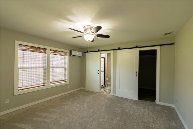 unfurnished bedroom with carpet floors, an AC wall unit, ceiling fan, and a barn door