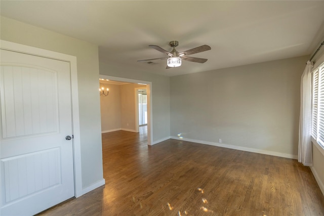 spare room with ceiling fan with notable chandelier and dark wood-type flooring