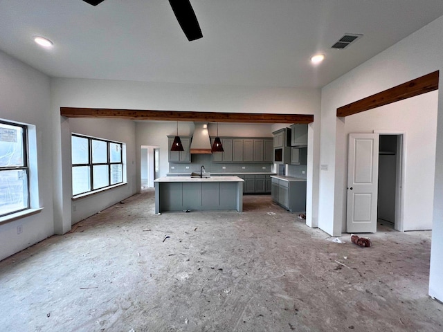 kitchen featuring sink, premium range hood, gray cabinetry, an island with sink, and decorative light fixtures