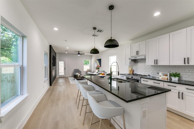 kitchen with decorative backsplash, ceiling fan, a kitchen island with sink, sink, and hanging light fixtures