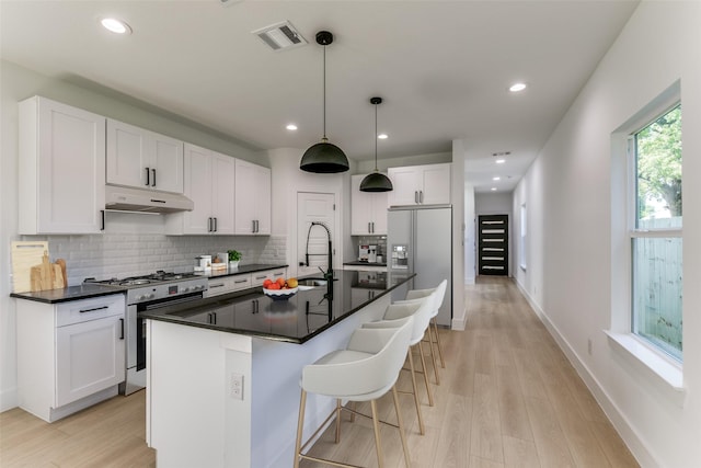 kitchen with sink, hanging light fixtures, high end stainless steel range oven, an island with sink, and white cabinets