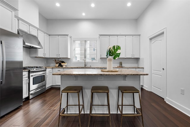 kitchen with white cabinets, a kitchen island, dark hardwood / wood-style flooring, stainless steel appliances, and light stone counters