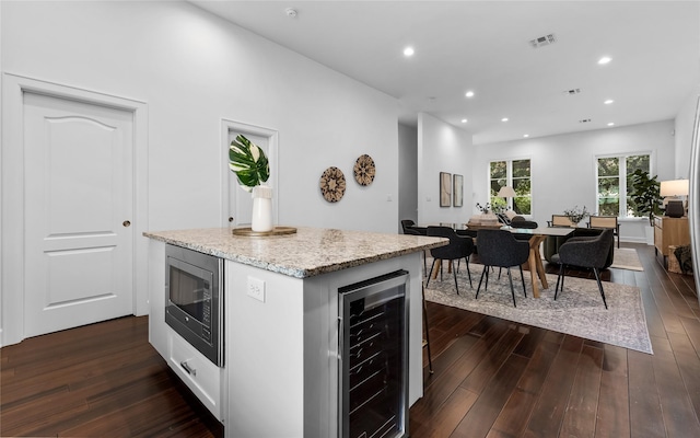 kitchen featuring stainless steel microwave, wine cooler, dark hardwood / wood-style flooring, white cabinetry, and a center island