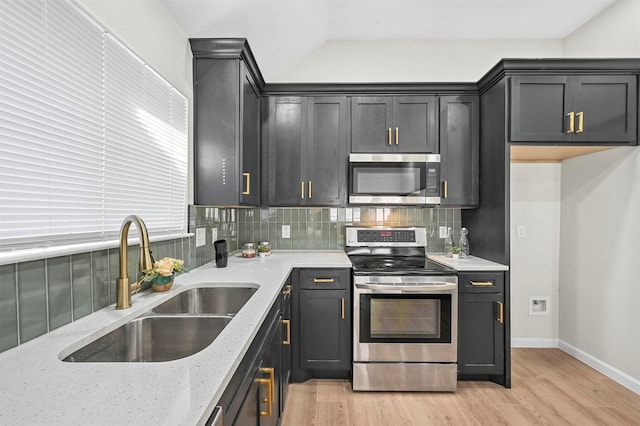 kitchen with light stone countertops, backsplash, stainless steel appliances, sink, and light hardwood / wood-style flooring