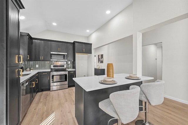 kitchen featuring a kitchen breakfast bar, backsplash, stainless steel appliances, light hardwood / wood-style flooring, and a kitchen island