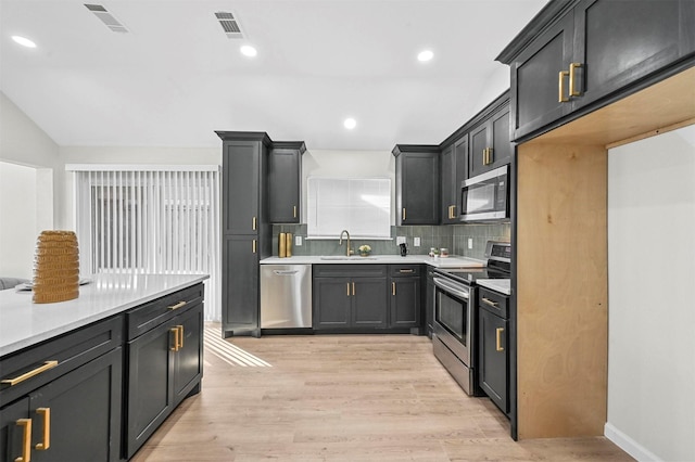 kitchen featuring backsplash, sink, vaulted ceiling, light wood-type flooring, and stainless steel appliances