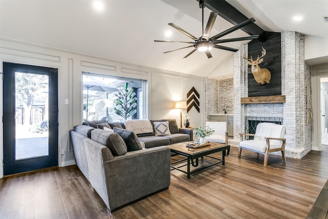 living room with ceiling fan, lofted ceiling with beams, wood-type flooring, and a brick fireplace