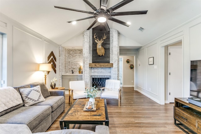 living room with ceiling fan, a fireplace, lofted ceiling, and light wood-type flooring