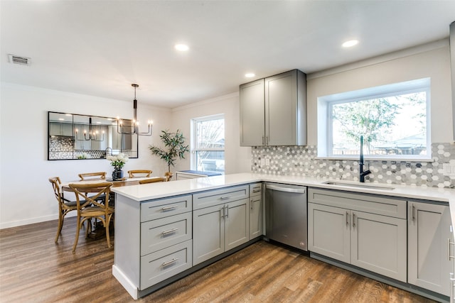 kitchen featuring kitchen peninsula, stainless steel dishwasher, gray cabinetry, sink, and decorative light fixtures