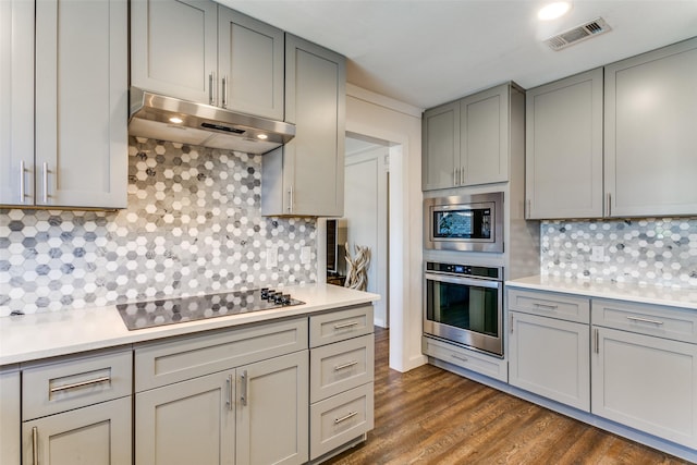 kitchen with decorative backsplash, stainless steel appliances, gray cabinets, and dark wood-type flooring