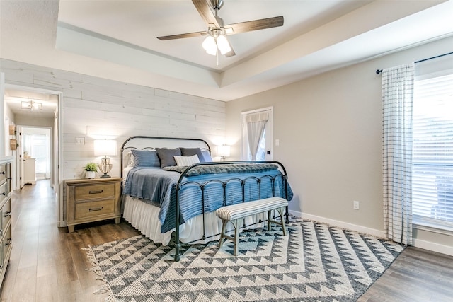 bedroom featuring ceiling fan, wood walls, dark wood-type flooring, and a tray ceiling