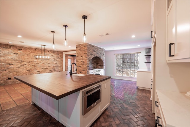 kitchen featuring pendant lighting, a kitchen island with sink, wooden counters, sink, and white cabinetry