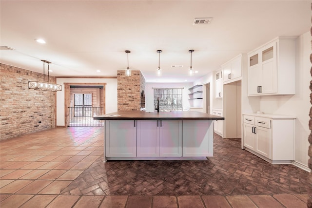 kitchen featuring white cabinets, decorative light fixtures, a healthy amount of sunlight, and an island with sink