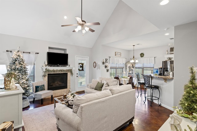 living room featuring ceiling fan with notable chandelier, dark tile patterned floors, a fireplace, and high vaulted ceiling