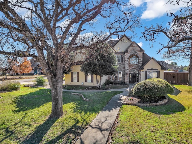 french country inspired facade featuring a front yard, stone siding, and stucco siding