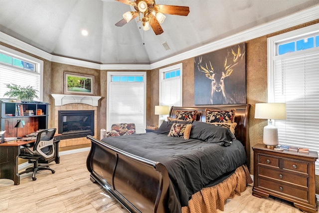 bedroom with vaulted ceiling, ceiling fan, crown molding, and a tiled fireplace