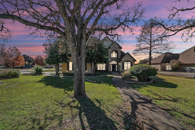 french country home with stone siding, a lawn, and stucco siding