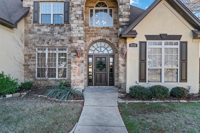 doorway to property featuring stone siding, roof with shingles, and stucco siding