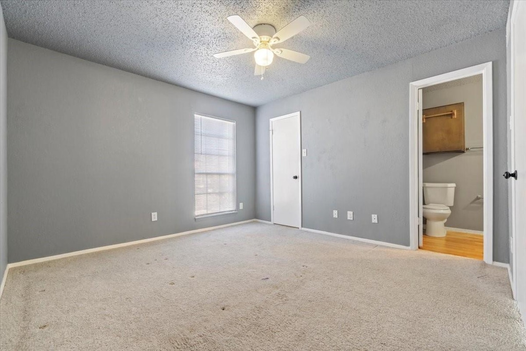 unfurnished bedroom with ceiling fan, light colored carpet, connected bathroom, and a textured ceiling