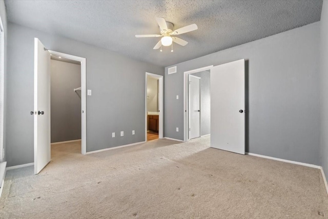 unfurnished bedroom with connected bathroom, ceiling fan, light colored carpet, a textured ceiling, and a walk in closet