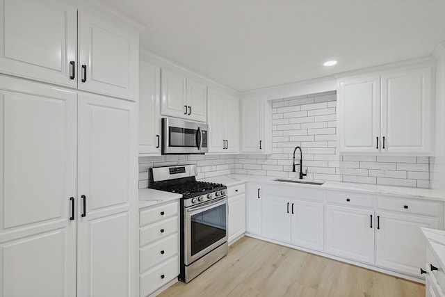 kitchen with tasteful backsplash, appliances with stainless steel finishes, sink, and white cabinets