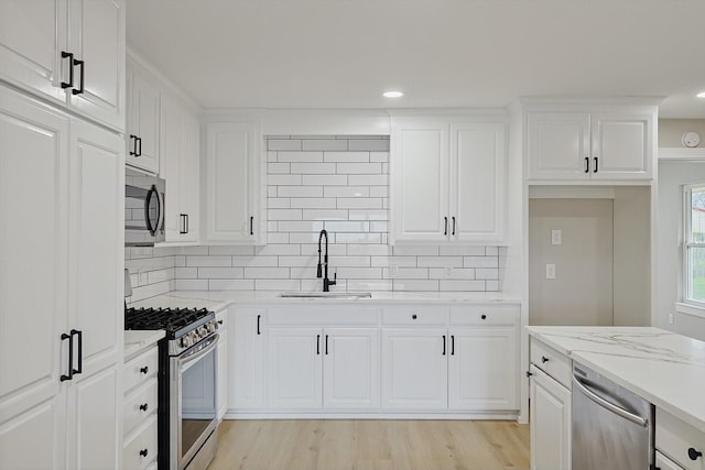 kitchen featuring light stone counters, stainless steel appliances, sink, and white cabinets