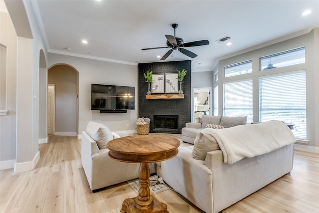 living room featuring crown molding, ceiling fan, a fireplace, and light hardwood / wood-style floors