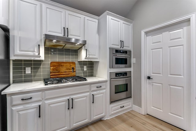 kitchen with decorative backsplash, light stone countertops, stainless steel appliances, light hardwood / wood-style flooring, and white cabinetry