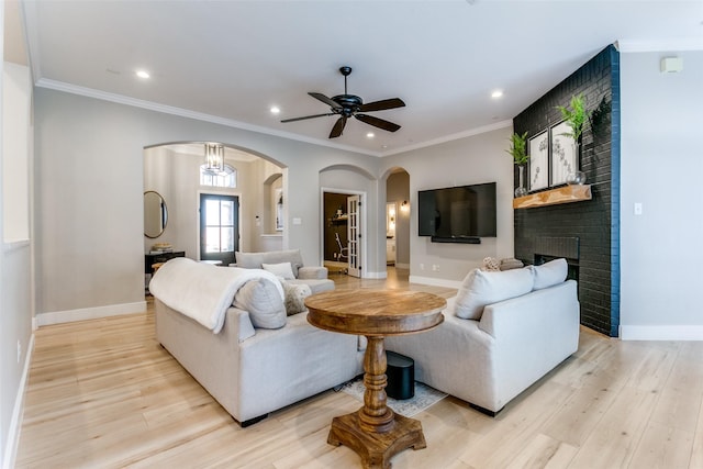 living room with a brick fireplace, light hardwood / wood-style flooring, ceiling fan, and ornamental molding