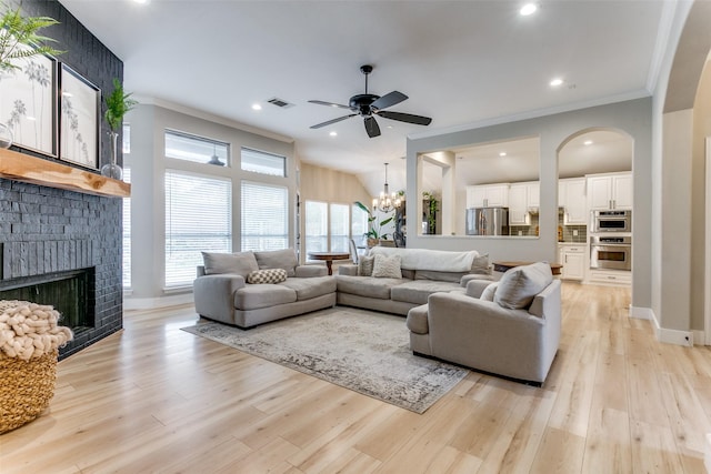 living room featuring ceiling fan with notable chandelier, light wood-type flooring, a brick fireplace, and ornamental molding