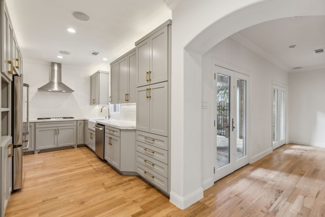 kitchen featuring wall chimney exhaust hood, light wood-type flooring, decorative backsplash, gray cabinets, and appliances with stainless steel finishes