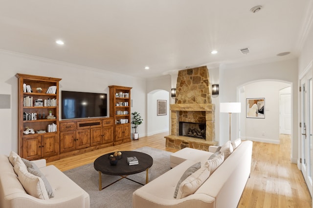 living room with ornamental molding, light hardwood / wood-style flooring, and a stone fireplace