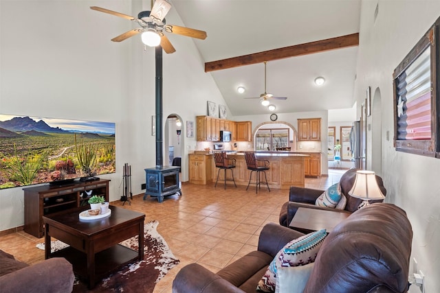 tiled living room featuring a wood stove, ceiling fan, beamed ceiling, and high vaulted ceiling