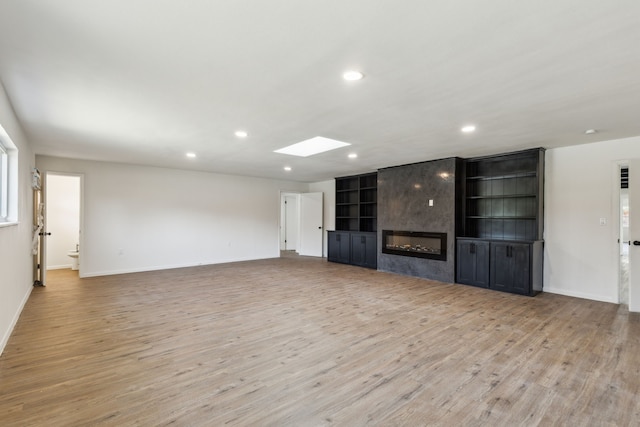 unfurnished living room featuring light hardwood / wood-style floors, built in features, a tile fireplace, and a skylight